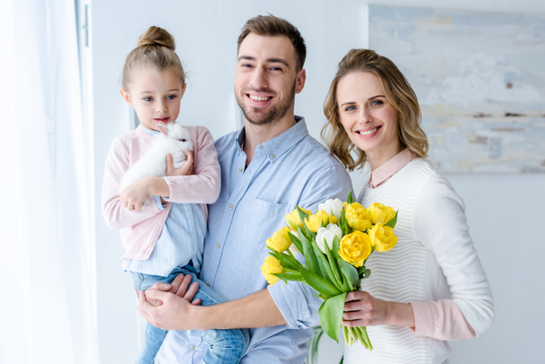 Familia feliz abrazando y sosteniendo conejito y tulipanes
 - Foto, Imagen