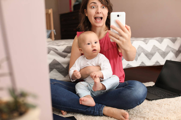 Young mother taking selfie with her cute baby at home - Foto, afbeelding