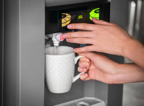 Woman filling cup from water cooler, closeup - Photo, image