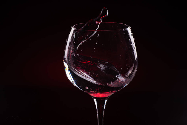 Red wine splashing out of a tall wine glass - Foto, afbeelding