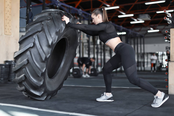 Young muscular woman flipping heavy tire in gym - Foto, Imagem