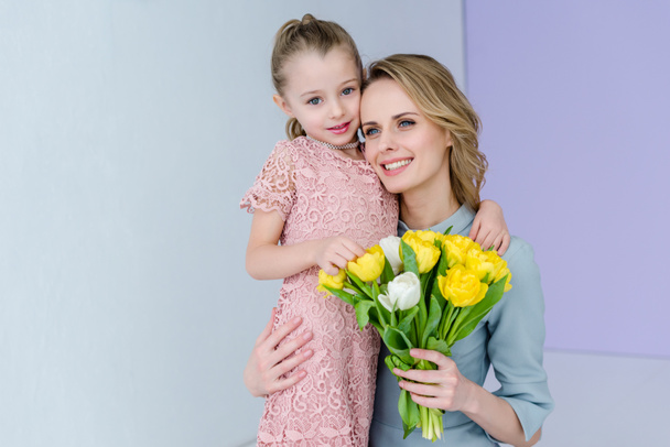 Woman holding bouquet and embracing cute daughter on women's day - Foto, immagini