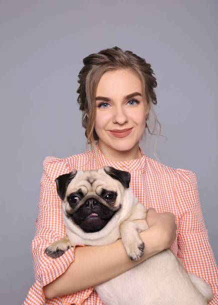 Young woman with cute pug dog on grey background. Pet adoption - Фото, изображение