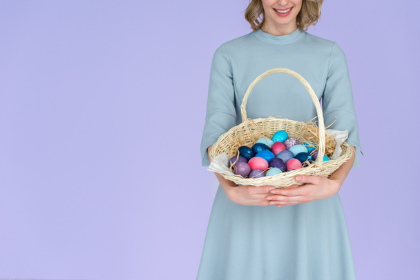 Жінка з розфарбованими великодніми яйцями в кошику ізольовані на фіолетовому
 - Фото, зображення