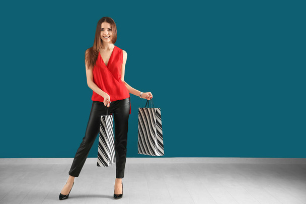 Young woman with shopping bags against color wall - Foto, Bild
