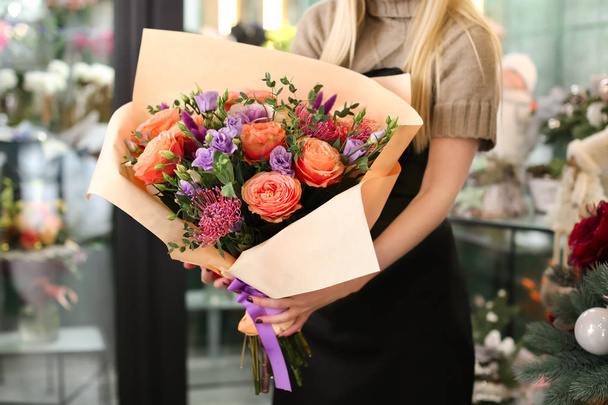 Female florist holding beautiful bouquet in flower shop - 写真・画像