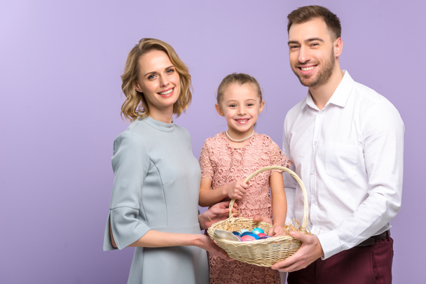 Parents and daughter with Easter basket with colored eggs isolated on violet - Photo, Image
