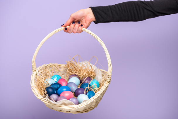 Woman holding Easter basket with colored eggs isolated on violet - Photo, Image