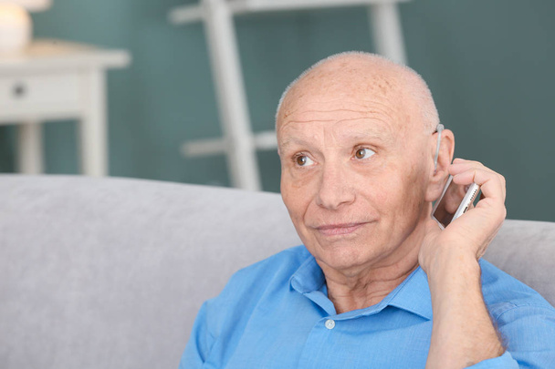 Senior man with hearing aid talking on phone indoors - Fotografie, Obrázek