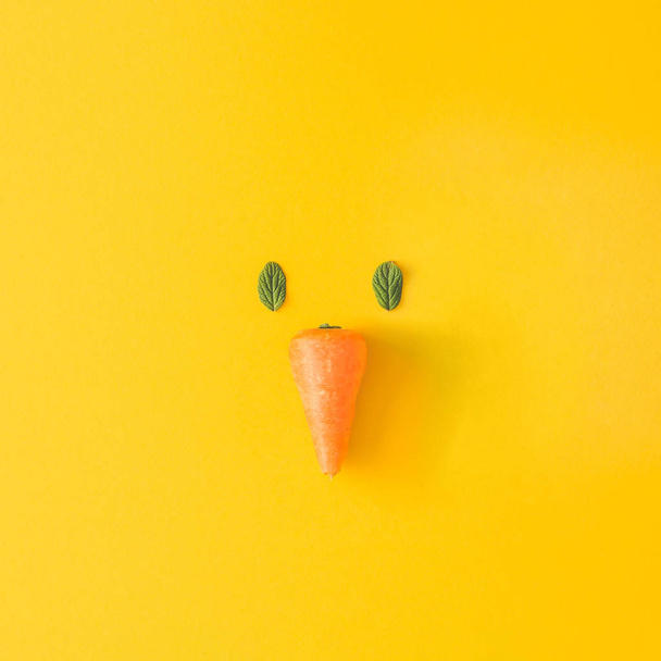 пасхальный цыпленок лицо из натуральных зеленых листьев и морковь на желтом фоне, Пасха минимальная концепция
 - Фото, изображение