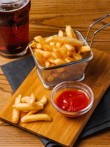 Antipasti patatine fritte in cesto, birra fredda e ketchup dolce serviti su tagliere di legno con tovagliolo grigio
 - Foto, immagini