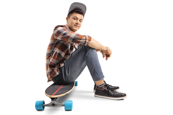 Teenage skater boy sitting on a longboard isolated on white background - 写真・画像