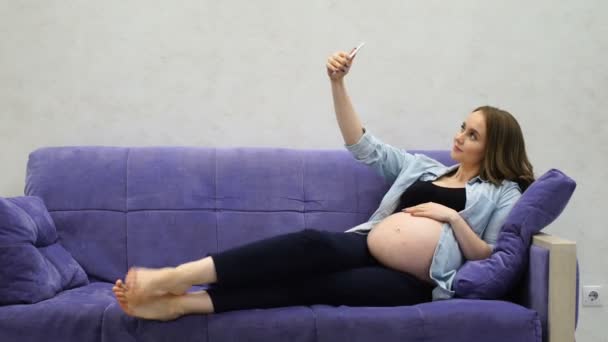 Bella donna incinta seduta sul divano in soggiorno selfie Dalet per i social network
. - Filmati, video