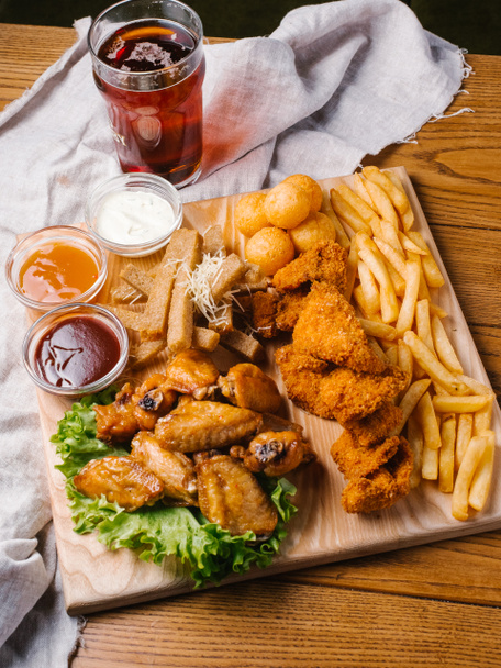Beer plate with chicken wings, chicken nuggets, garlic toasts and french fries with different sauces, lettuce served on wooden cutting board with dark beer glass - Fotografie, Obrázek