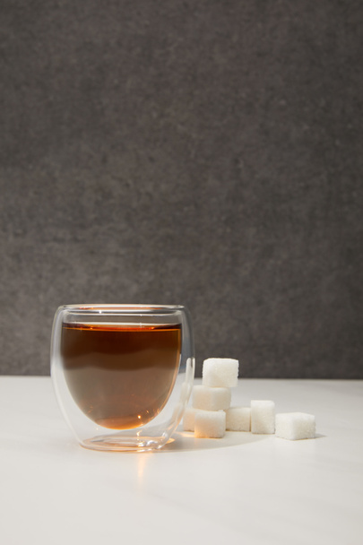 vergrote weergave van glazen beker met verse biologische kruiden thee en suiker kubussen op grijs   - Foto, afbeelding