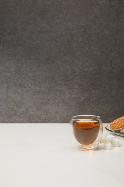 fresh hot tea in glass cup, sugar cubes and tasty cookies on grey  - Fotó, kép