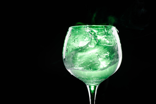 Splashing water in the wine glass with green background - Foto, imagen