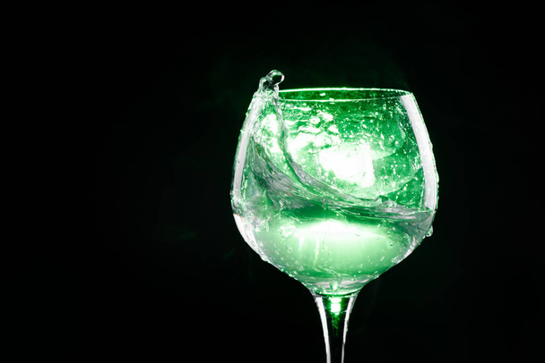 Splashing water in the wine glass with green background - Foto, imagen