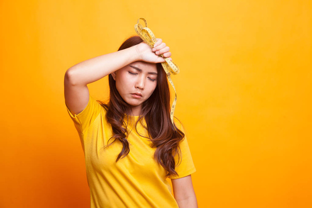 Unhappy young Asian woman with measuring tape in yellow dress - Foto, Bild