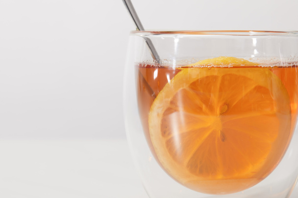 Крупный план стеклянной чашки со свежим горячим чаем, ложкой и ломтиком лимона на сером
 - Фото, изображение