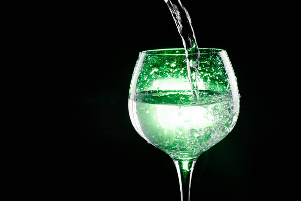 Pouring water in the wine glass with green background - Foto, imagen