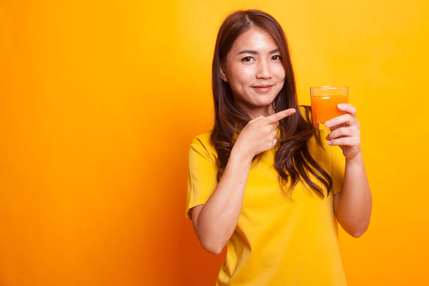 Young Asian woman point to orange juice in yellow dress - Foto, afbeelding
