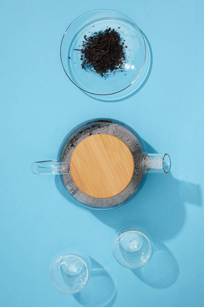 pohled shora konvice s čerstvý čaj, prázdné šálky a suché bylinné čaje v misce na modré  - Fotografie, Obrázek