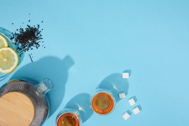 vue du dessus de thé frais dans les tasses et théière, cubes de sucre, tisane sèche et citron tranché sur bleu
  - Photo, image
