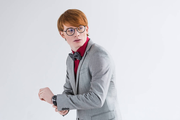 Young male fashion model in eyeglasses adjusting wristwatch isolated on grey - Foto, Bild