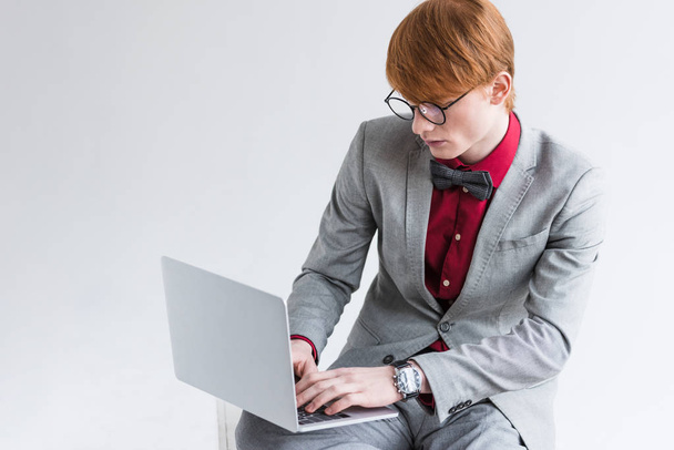 Male fashion model dressed in suit using laptop isolated on grey - Valokuva, kuva