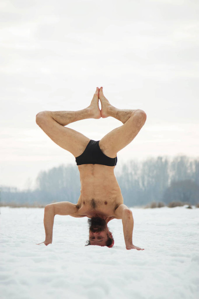 A middle-aged man is engaged in yoga on a frozen river. Shirshas - Foto, Bild