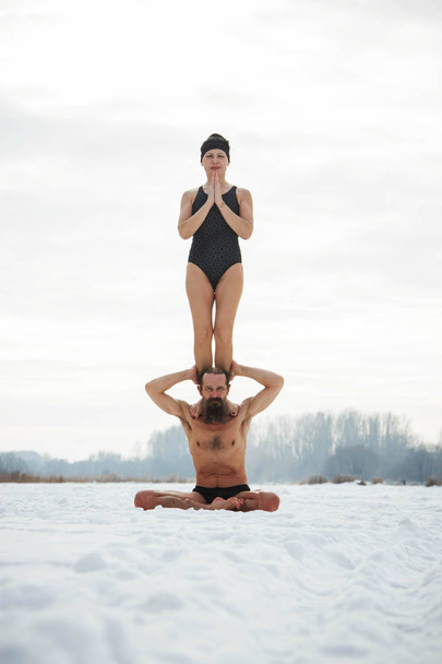 A man and a middle-aged woman practicing yoga on a frozen river. - Foto, Bild
