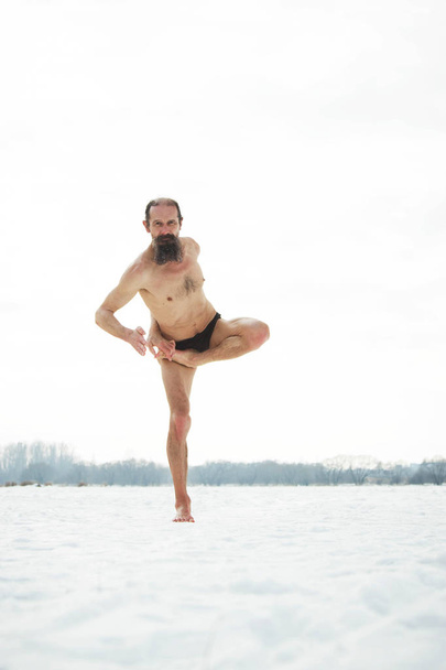 A middle-aged man is engaged in yoga on a frozen river. Vrishasa - Photo, image