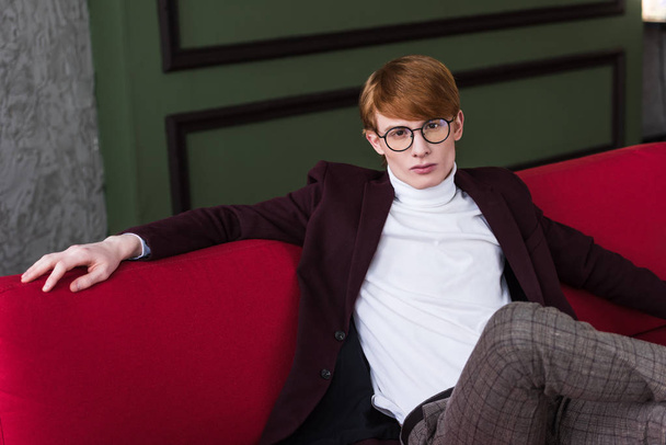 Young male fashion model in eyeglasses sitting on couch - Φωτογραφία, εικόνα