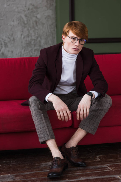 Male model in eyeglasses dressed in jacket sitting on couch  - Fotoğraf, Görsel
