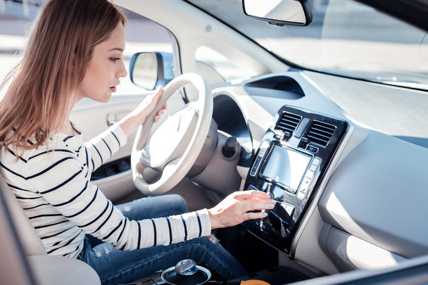 Occupied interested woman sitting in the car holding touching control panel. - 写真・画像