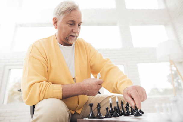 高齢者のカップルは、自宅のチェスをプレイします。彼らは、喜びと喜びと遊ぶ。彼らは大きな窓のリビング ルームに座っています。 - 写真・画像