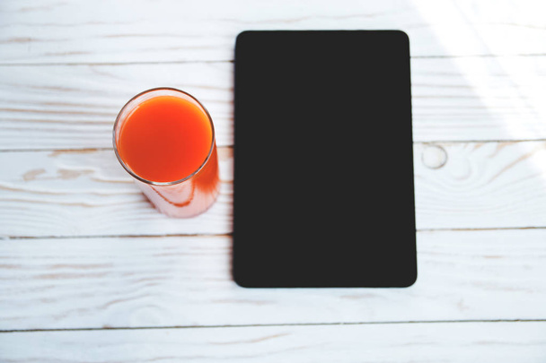 orange carrot juice and digital device on a white wooden background - Zdjęcie, obraz