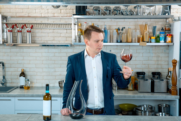 Koncentrovaná mladý muž sommelier, degustace a při pohledu na červené víno ve skle - Fotografie, Obrázek
