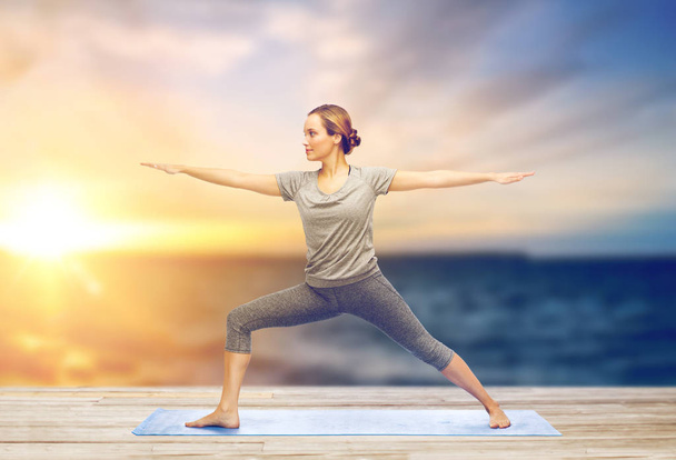 woman making yoga warrior pose on mat - Photo, Image