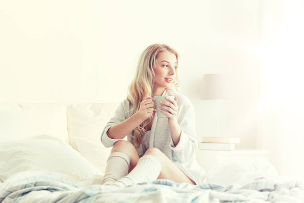 ευτυχισμένη γυναίκα με καφέ στο κρεβάτι στο σπίτι - Φωτογραφία, εικόνα