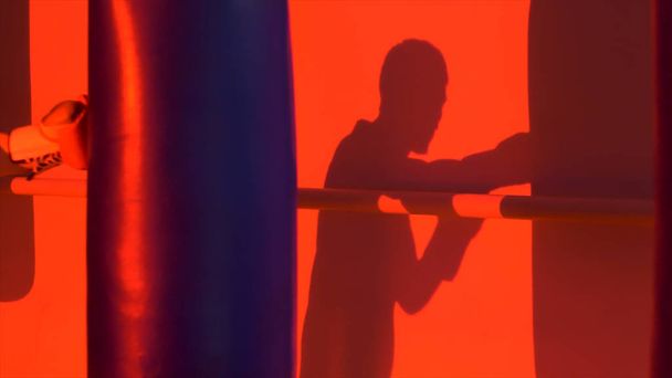 Silhouette or shadow of a boxer punching a punching bag close up, red light background. Silhouette of young male boxer hitting punching bag on red background. Man athlete standing and boxing. - Fotoğraf, Görsel