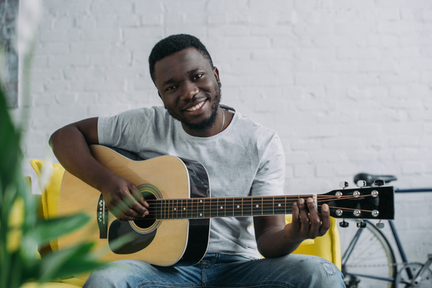 young african american man playing guitar and smiling at camera - Foto, afbeelding