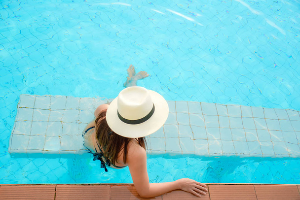 Summer Vacations.  Lifestyle woman happy with bikini and big hat relaxing on the swimming pool, travel near the sea and beach in holiday. Summer Concept - 写真・画像