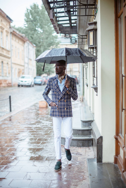 Confident young African man in a stylish suit with umbrella on city street - Foto, imagen