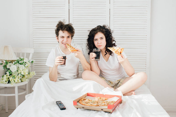 Пара смотрит телевизор в постели и ест пиццу
 - Фото, изображение
