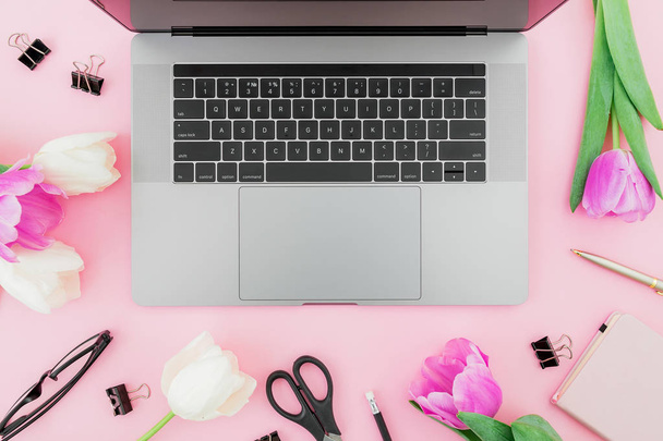 Office desk with laptop, white tulips, glasses, pen and scissors on pink background. Flat lay. Top view. Freelancer composition with copy space. - Photo, Image