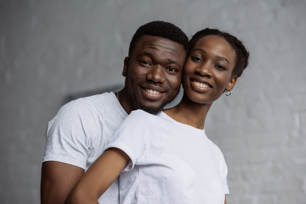 счастливая молодая африканская американская пара в белых футболках улыбающаяся в камеру
 - Фото, изображение