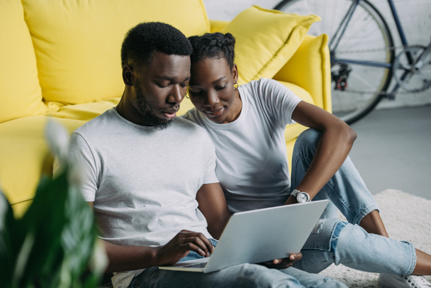young african american couple in white t-shirts using laptop together at home - Photo, Image