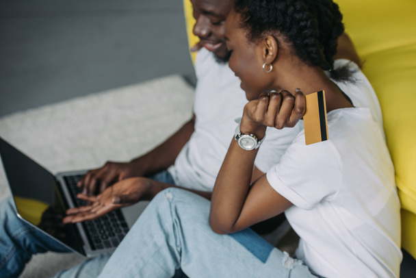 bijgesneden schot van glimlachen jonge Afrikaanse Amerikaanse echtpaar met laptop en creditcard online winkelen  - Foto, afbeelding